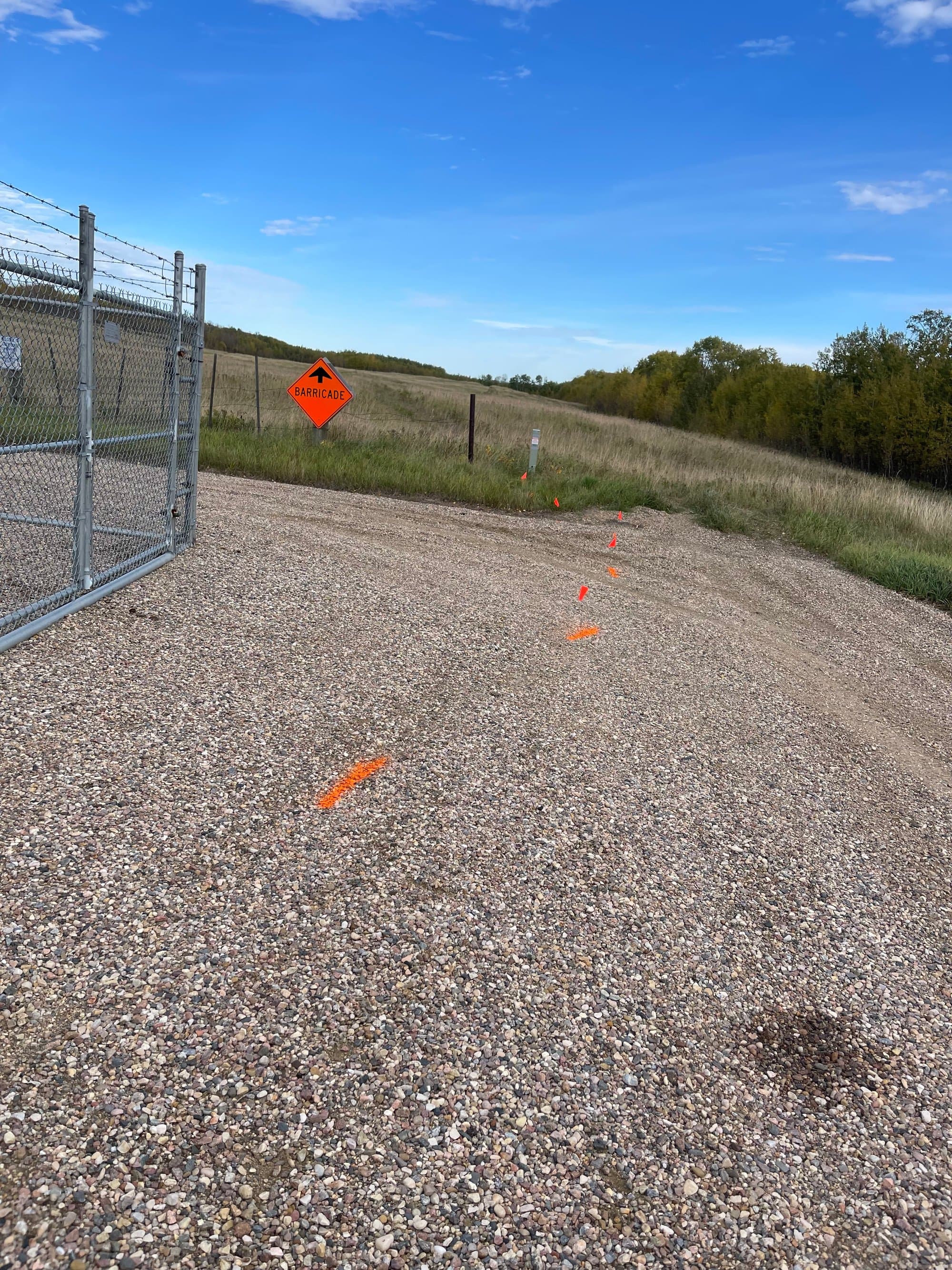 Gated gravel access road marked with locate flags