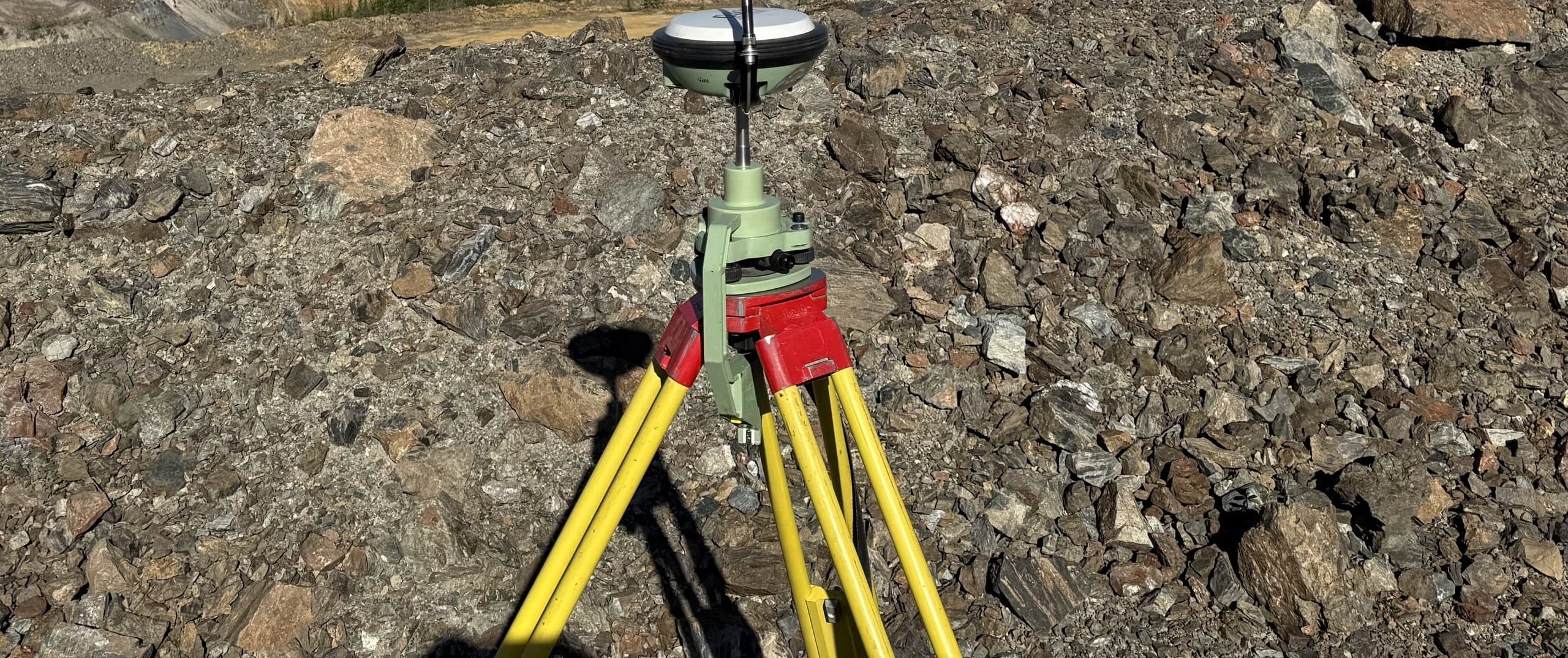 Survey-grade GNSS receiver set up over rocky broken ground above a waterbody