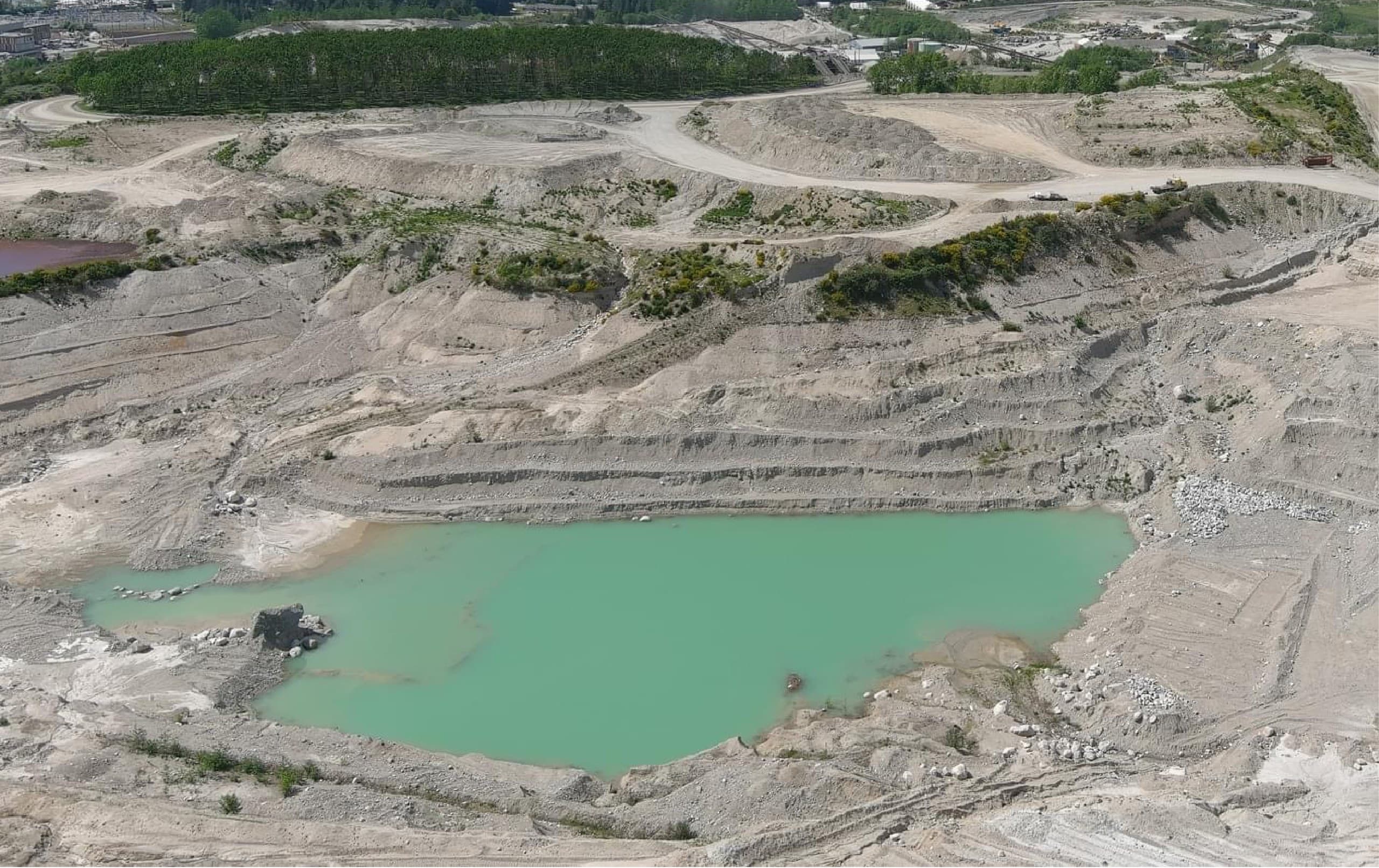 Aerial view of a working gravel pit with benches, haul roads and a settling pond