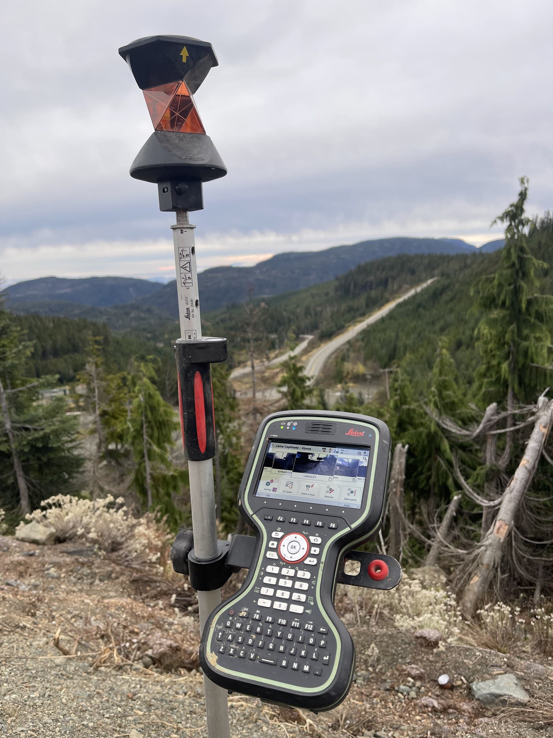 Prism pole and field controller on a corridor survey above a valley road