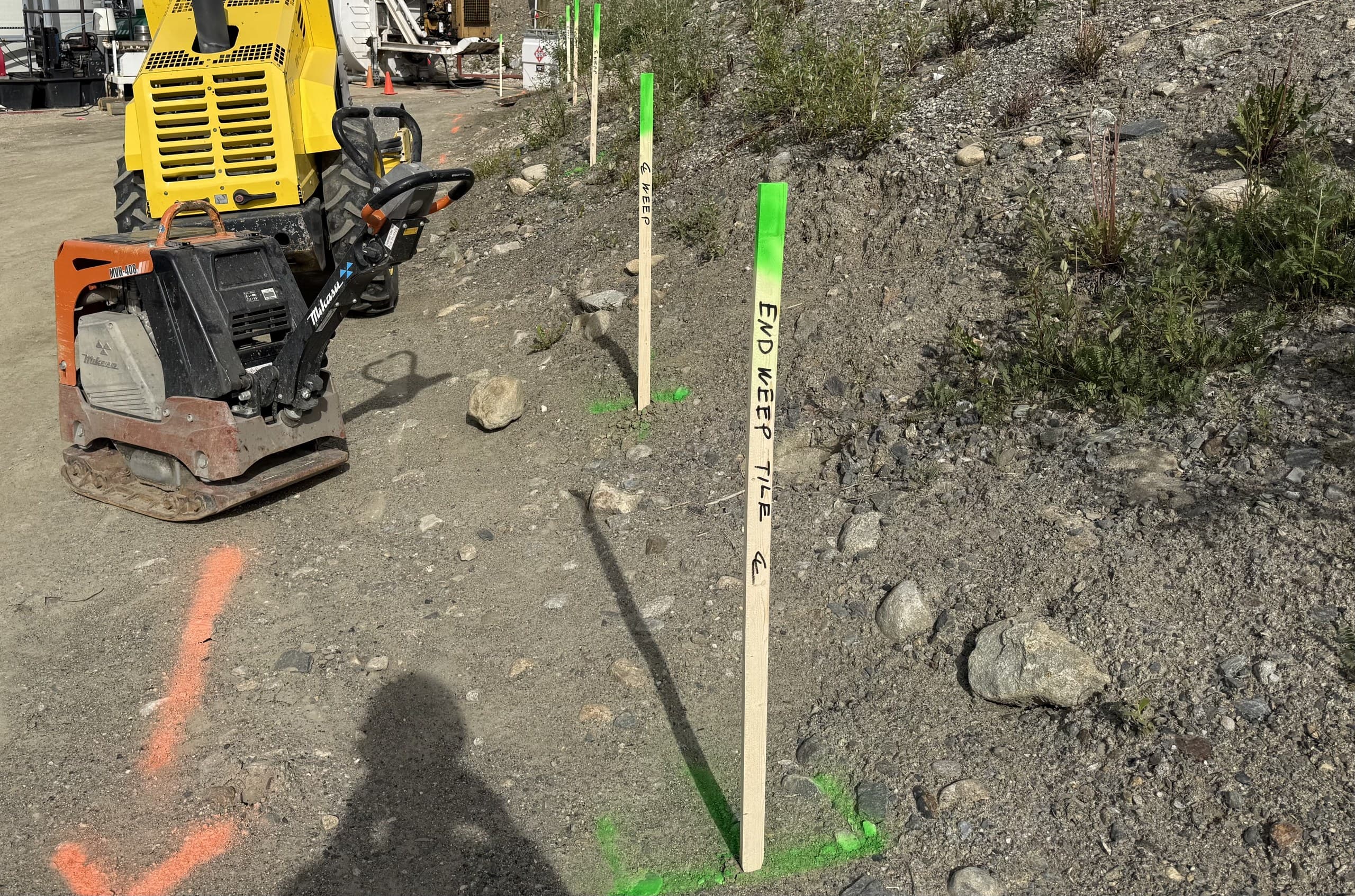 Servicing layout stakes and paint marks along a graded slope