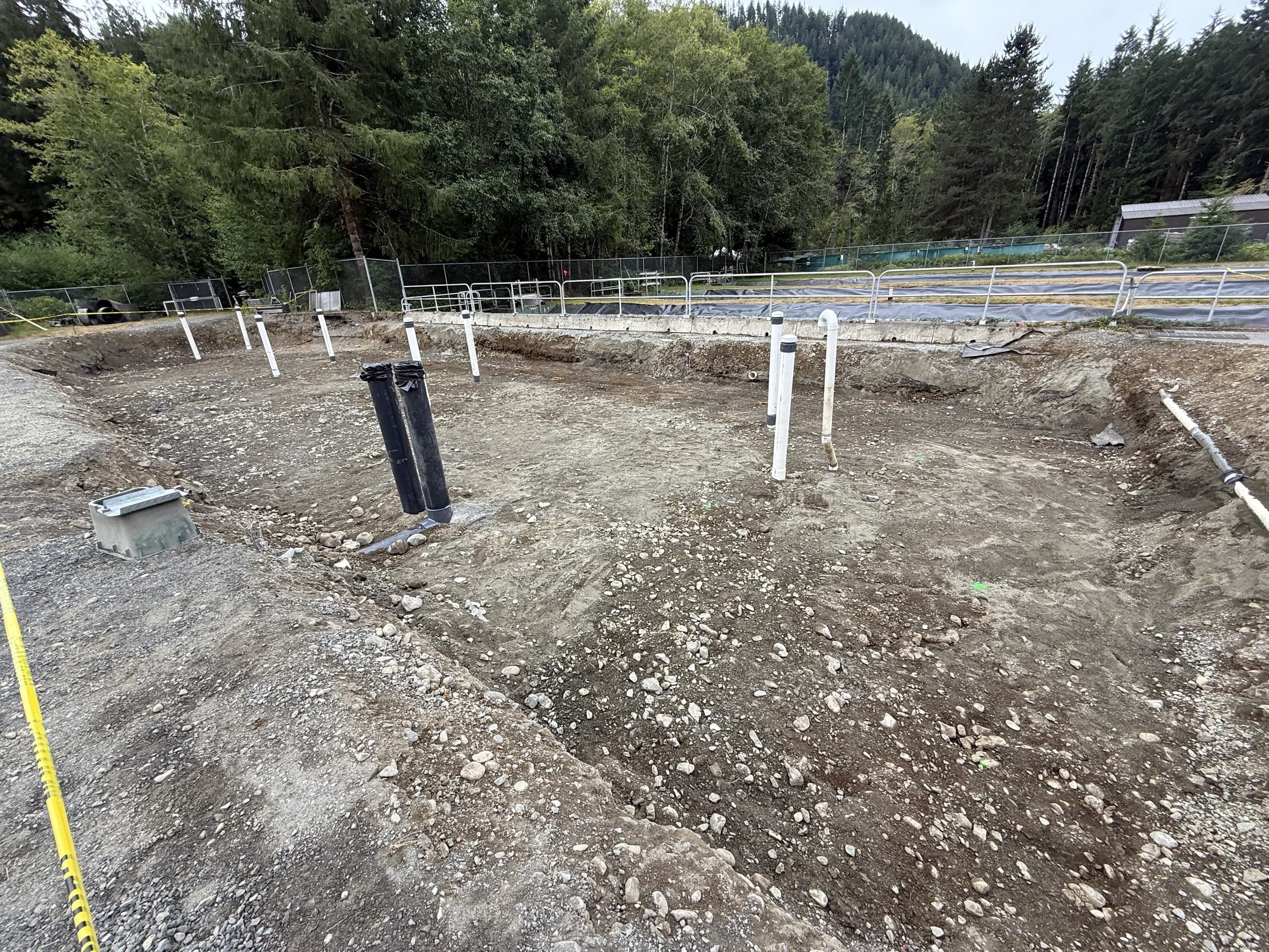 Excavated site with services roughed in, forest hillside behind
