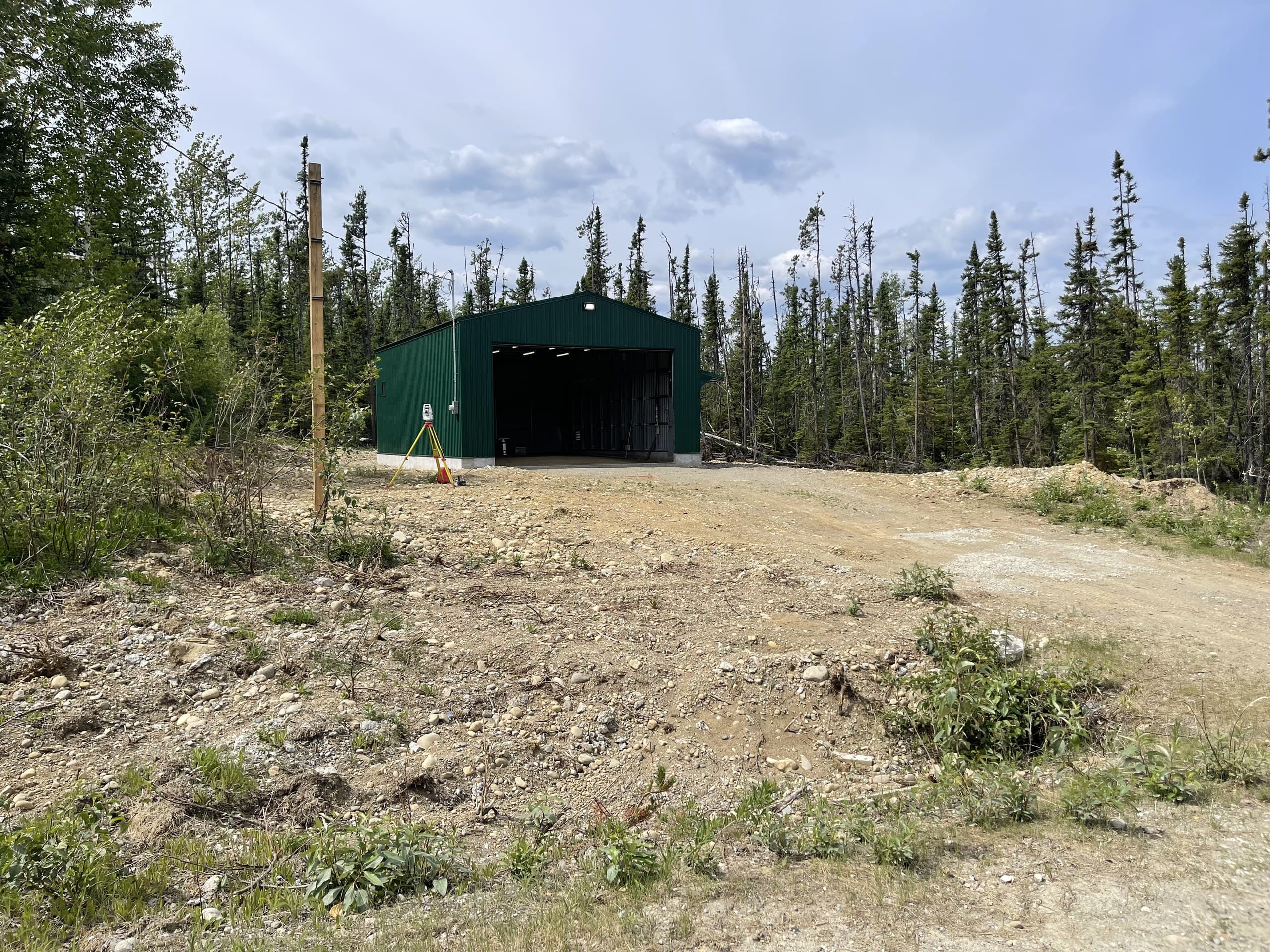 Steel building on a freshly cleared gravel site with a survey tripod at the entrance