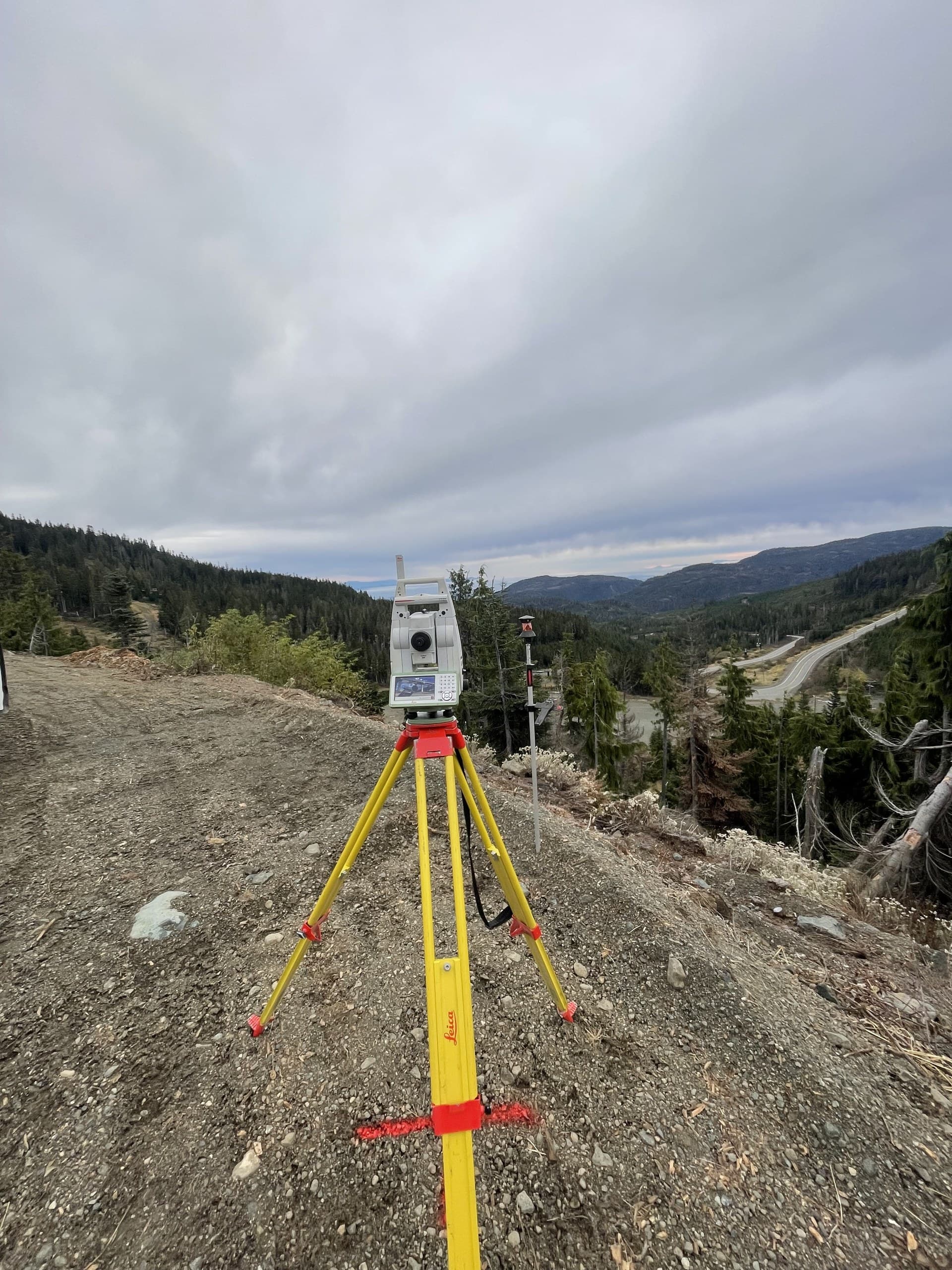 Robotic total station on a gravel bench overlooking a mountain highway corridor