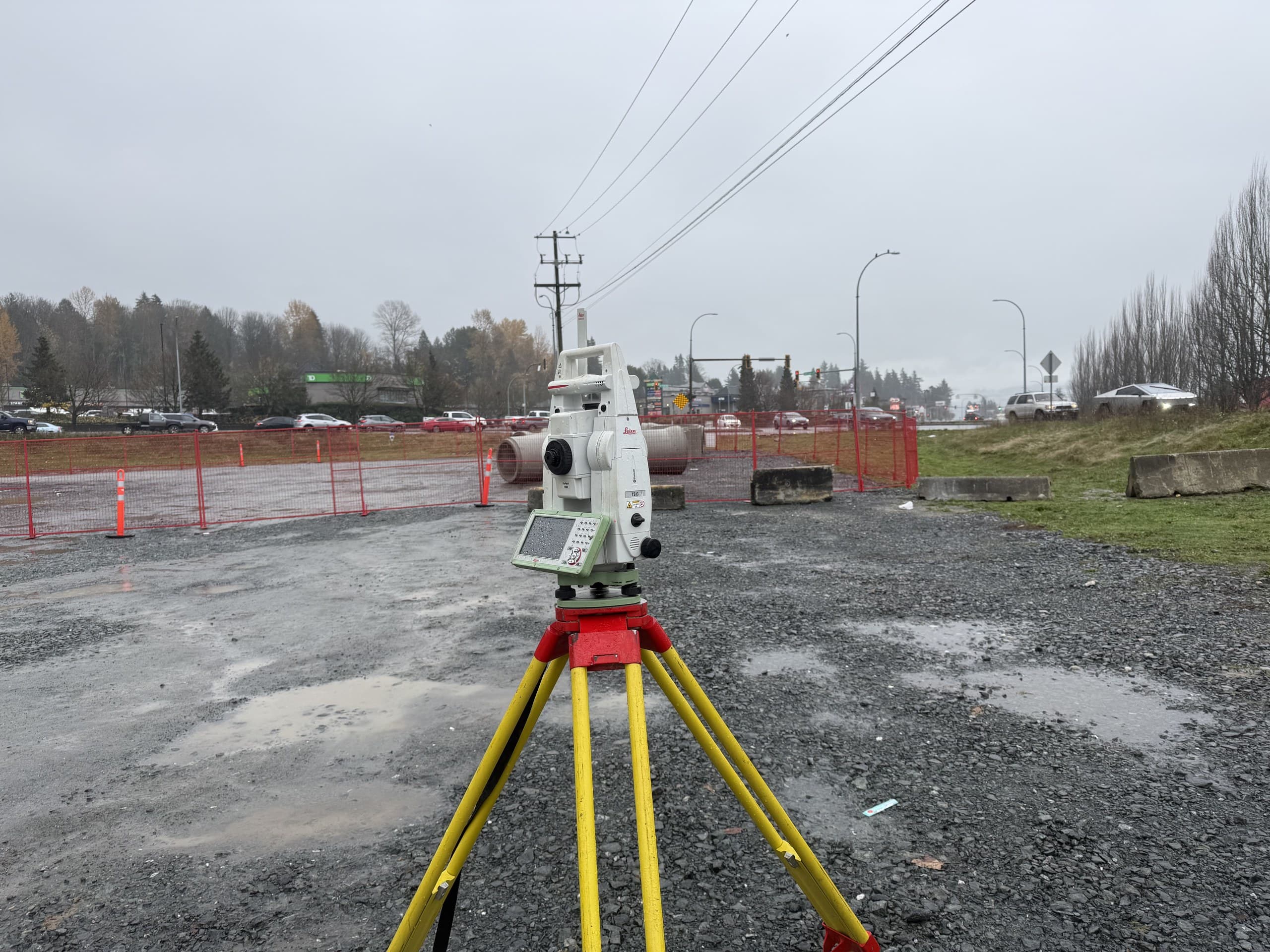Robotic total station on a fenced commercial site beside a busy highway corridor