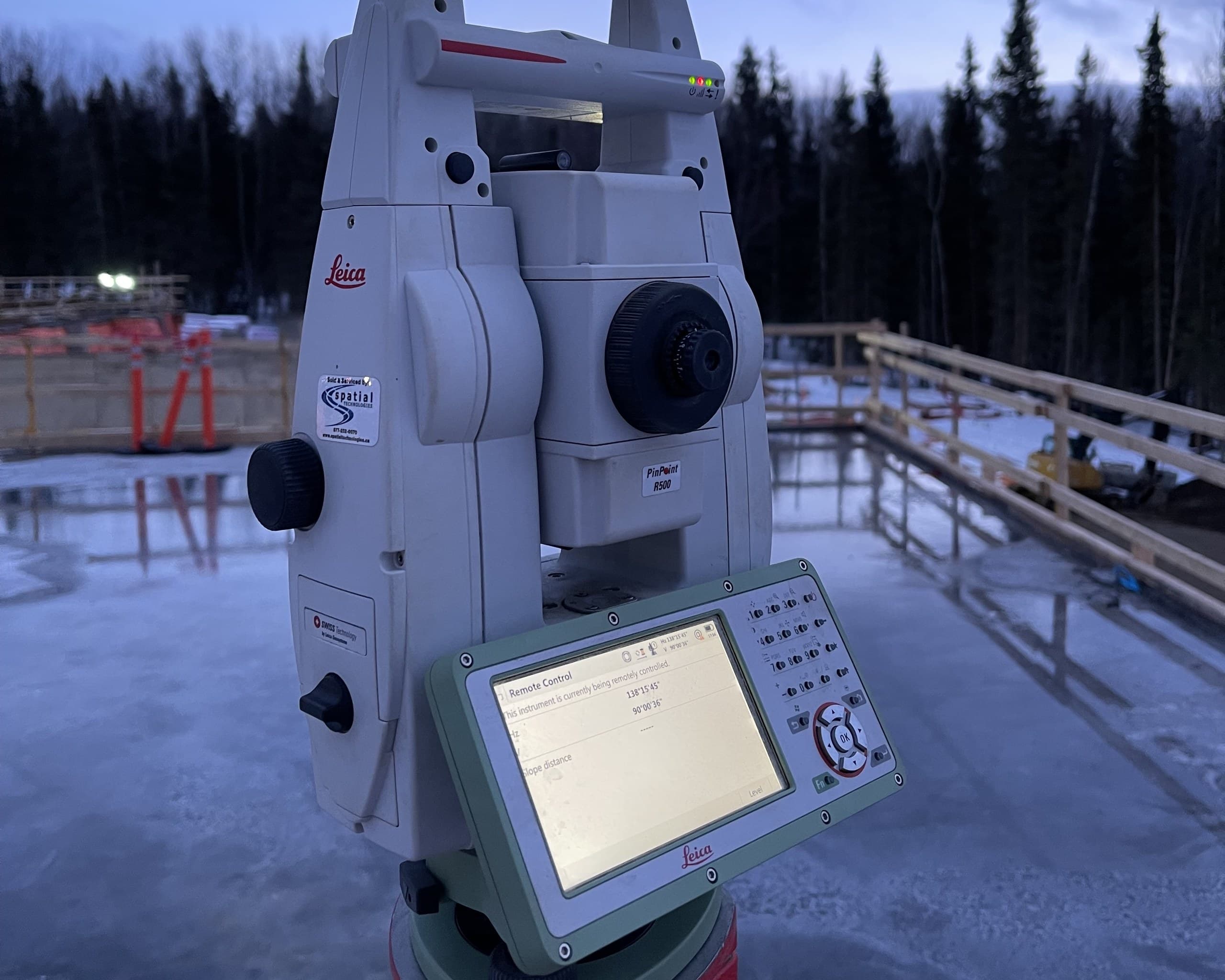 Robotic total station at winter dusk on a scaffolded construction site
